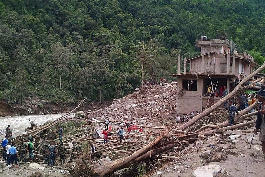 In this photograph taken using a cellphone, Nepalese residents and rescue personnel stand among debris at the site of a landslide on the Sukoshi river in Sindhupalchowk district northeast of Kathmandu on Aug 3, 2014.&nbsp;Rescuers in Nepal struggled 
