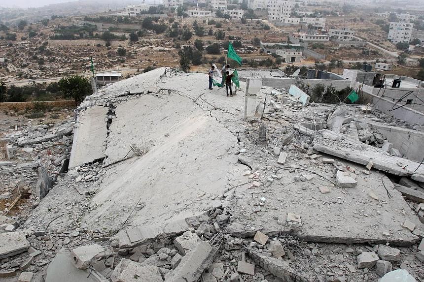 Palestinians raise Islamist Hamas movement flags on the top of what remains of the house of Hussam Qawasmeh, named by Israel as one of the suspects in the murder of three kidnapped Israeli teenagers a month ago.&nbsp;The Israeli army said on Monday i