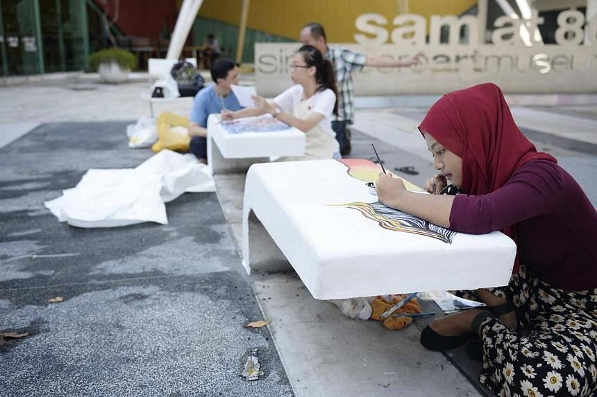 Nur Syuhada, 17, a student from the Nanyang Academy of Fine Arts putting her touches on public benches along Queen Street. -- ST PHOTO: DESMOND LIM