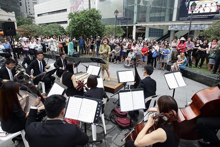 A member of the public tries her hand at conducting Ding Yi Music Company at an open-air lunchtime concert in Raffles Place.