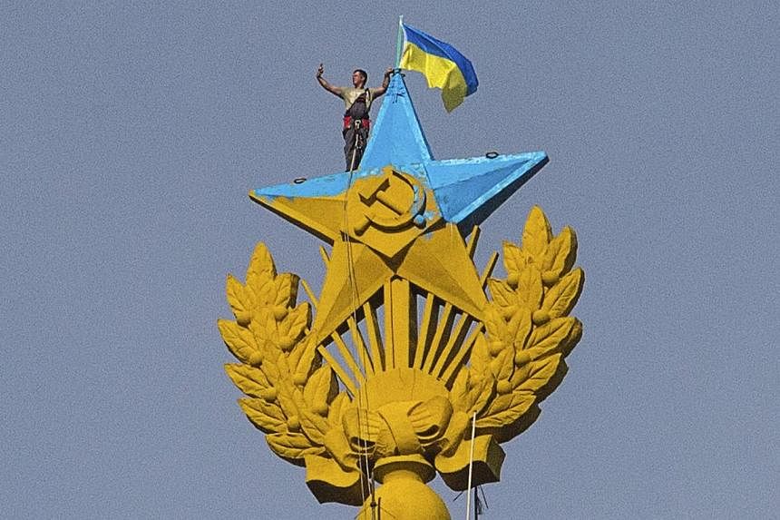 A man takes a selfie as he stands with a Ukrainian flag on a Soviet-style star re-touched with blue paint so it resembles the yellow-and-blue national colours of Ukraine, atop the spire of a building in Moscow on Aug 20, 2014.&nbsp;-- PHOTO: REUTERS