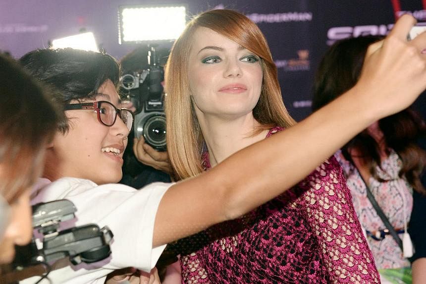 Hollywood actress Emma Stone (right) posing for a selfie with a fan on the red carpet during the film premiere of The Amazing Spider-Man 2: Rise of Electro at Marina Bay Sands in Singapore on 27 March 2014. -- PHOTO: BERITA HARIAN FILE
