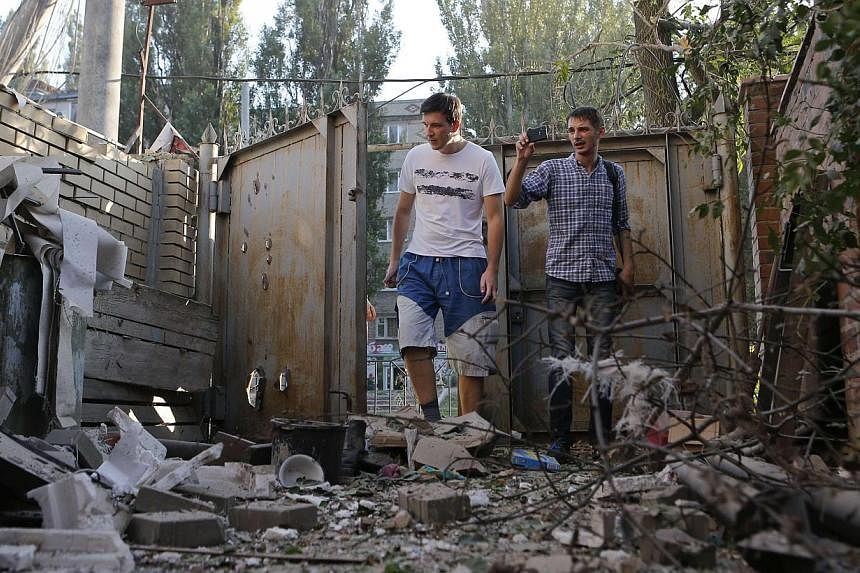 People walk in front of a building damaged by, what locals say, was recent shelling by Ukrainian forces in Donetsk on August 20, 2014. -- PHOTO: REUTERS