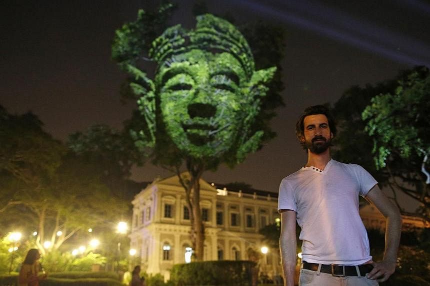 French artist Clement Briend poses with his photographic light installation Divine Trees, which features images of divine figures highly revered in Asian cultures projected on trees towering over bystanders, during a media preview of the Singapore Ni