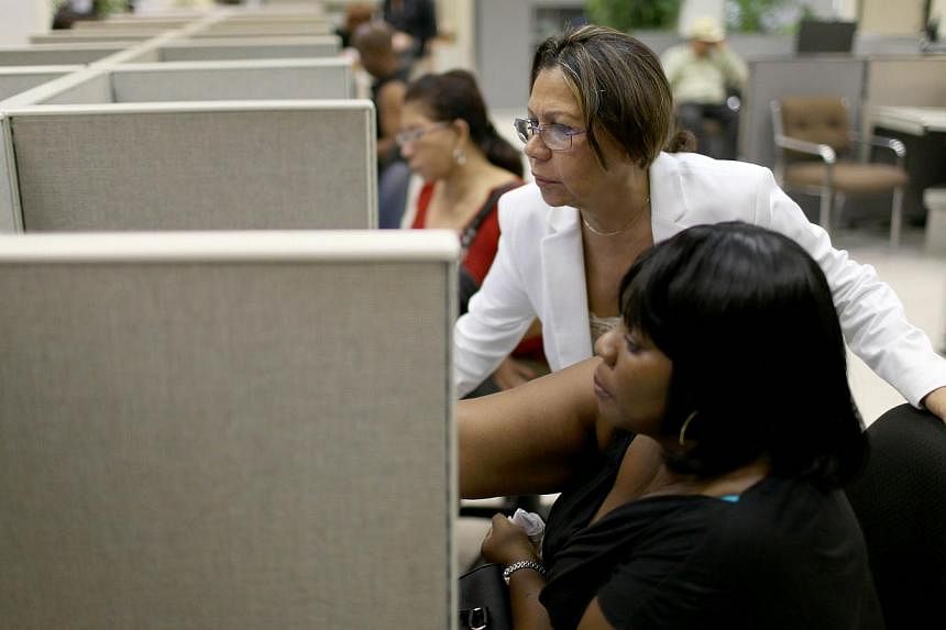 A woman helps a job seeker as she looks for job opportunities on the computers at CareerSource Florida on Aug 1, 2014 in Miami, Florida. -- PHOTO: AFP