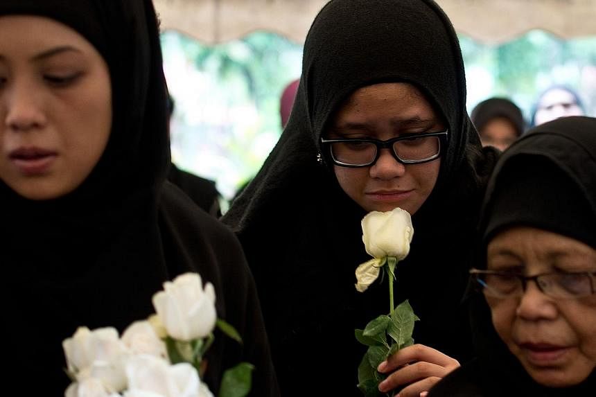 Nur Diyana Yazeera (centre), daughter of Malaysia Airlines MH17 chief stewardess Dora Shahila Kassim, holds a white rose during her mother's burial ceremony in Kuala Lumpur on Aug 22, 2014.&nbsp;The family of MH17 chief stewardess Dora Shahila Kassim