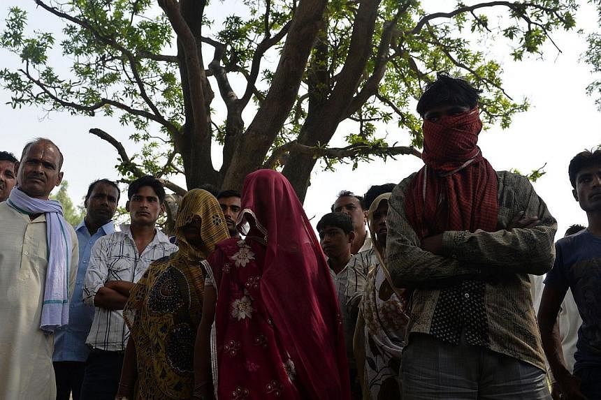 In this file photograph taken on May 31, 2014, the mothers of gang-rape victims (centre, with shawls covering their faces) and villagers stand in front of the tree where the bodies of the two girls were found hanging, in Katra Shahadatgunj in Badaun 