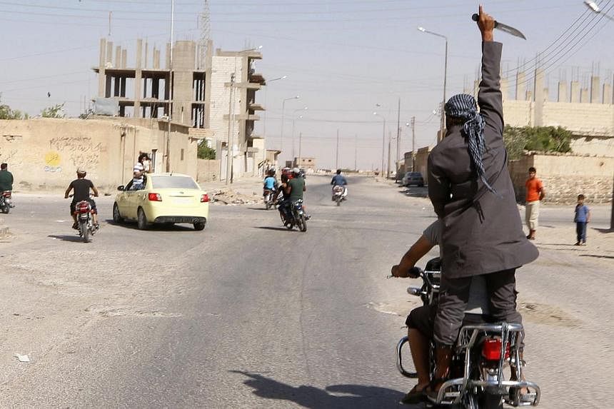 A man holds up a knife as he rides on the back of a motorcycle touring the streets of Tabqa city with others in celebration after Islamic State militants took over Tabqa air base, in nearby Raqqa city August 24, 2014. Islamic State militants stormed 