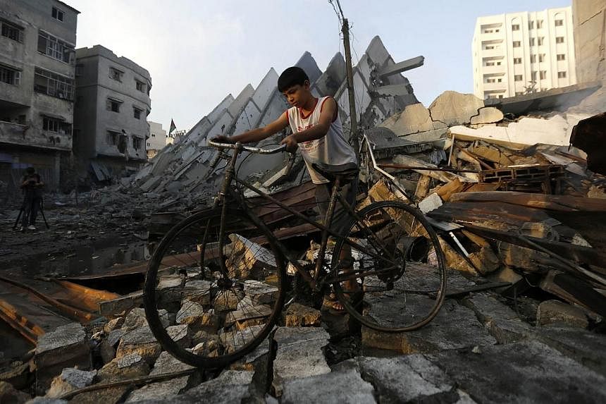 A young Palestinian walks with his bicycle over the remains of Al-Basha, a building that was destroyed by an Israeli air strike in Gaza City on Tuesday, Aug 26, 2014.&nbsp;The Palestinians have reached agreement with Israel on a "permanent" ceasefire
