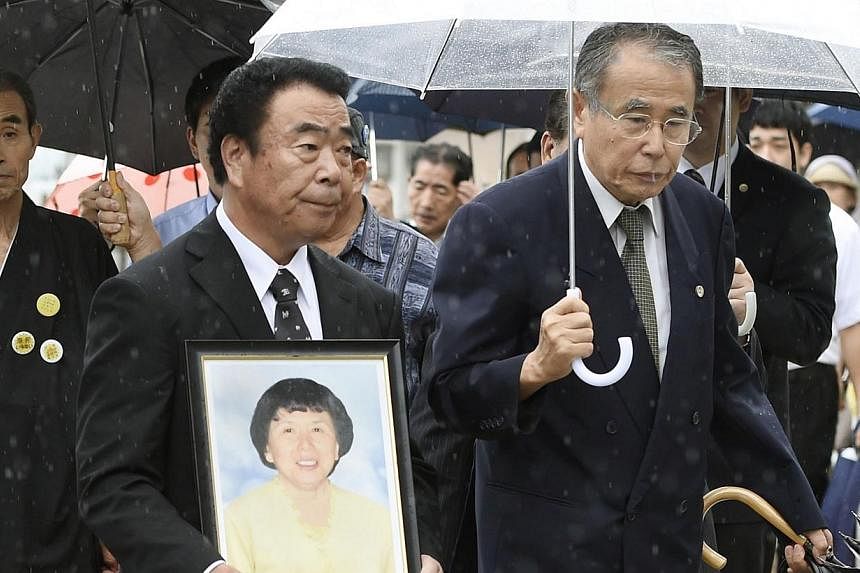 Mikio Watanabe, holding a portrait of his late wife Hamako, walks into the Fukushima District Court in Fukushima. -- PHOTO: REUTERS