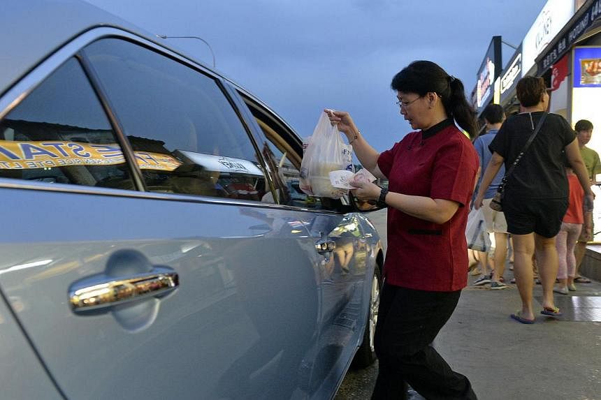An employee of Five Star Chicken Rice's outlet in Cheong Chin Nam Road handing over pre-ordered food and change to a drive-through customer. For restaurants, the drive-through is an alternative to home deliveries, which they are unable to provide due
