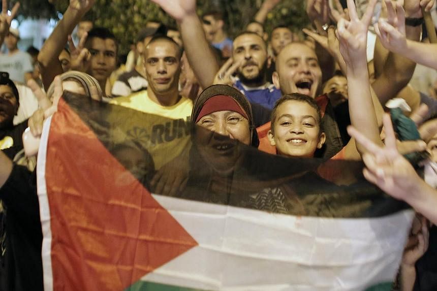 Palestinians flash the sign of victory wave a national flag as they celebrate in the streets in East Jerusalem the long-term truce agreed between Israel and the Palestinians on Aug 26, 2014. -- PHOTO: AFP&nbsp;