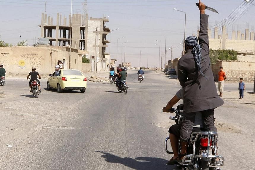 A man holds up a knife as he rides on the back of a motorcycle touring the streets of Tabqa city with others in celebration after Islamic State militants took over Tabqa air base, in nearby Raqqa City on Aug 24, 2014. -- PHOTO: REUTERS