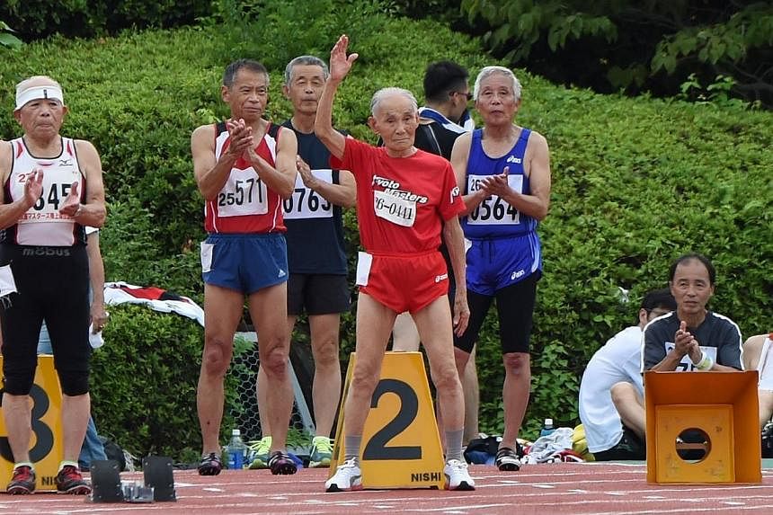 Japanese sprinter Hidekichi Miyazaki (centre) raises his hand when he is introduced on the start line for the men's 100m dash at a Japan Masters Athletics competition in Kyoto on Aug 3, 2014. -- PHOTO: AFP