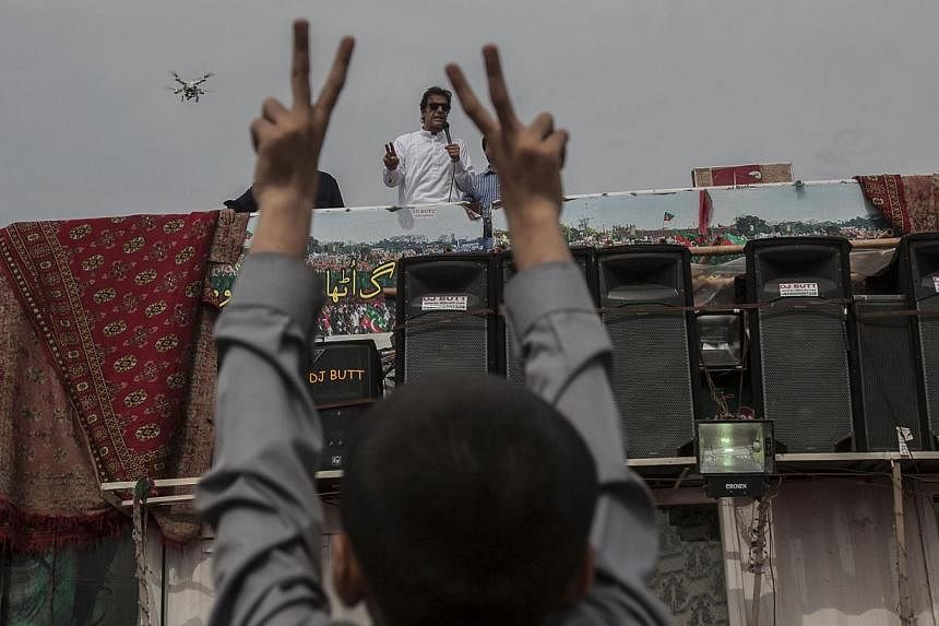 Imran Khan, chairman of the Pakistan Tehreek-e-Insaf political party, addresses supporters while a boy gestures in front of the Parliament house building during the Revolution March in Islamabad on August 28, 2014. He told his supporters that talks t