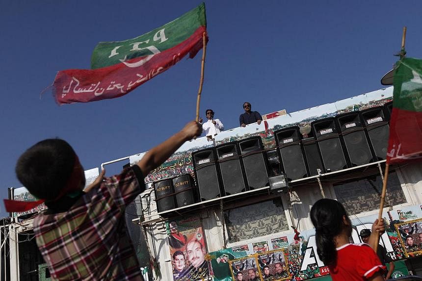 Mr Imran Khan, chairman of the Pakistan Tehreek-e-Insaf (PTI) political party, addresses supporters as children wave PTI's flag, in front of the Parliament building during the Revolution March in Islamabad on August 29, 2014. Former cricketer Imran K