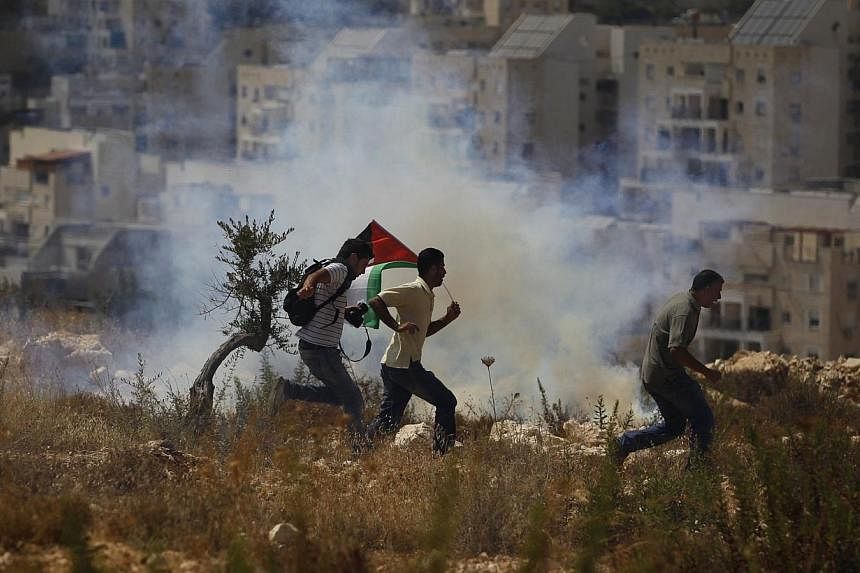 Palestinian protesters and a photographer run from tear gas fired by Israeli soldiers during clashes in the West Bank village of Bilin near Ramallah on Aug 29, 2014.&nbsp;Israel announced plans on Sundaym Aug 31, to expropriate 400ha of Palestinian l