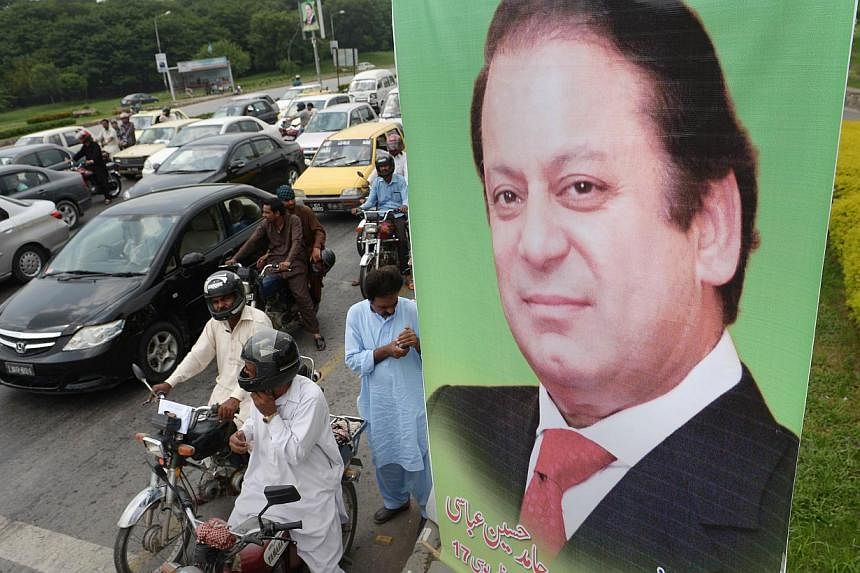 Pakistani commuters wait at traffic lights alongside a poster of Prime Minister Nawaz Sharif on a highway in Islamabad on August 25, 2014.&nbsp;Sharif on Saturday dismissed a political crisis triggered by protests aimed at unseating his government as