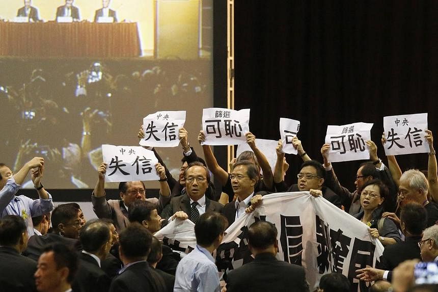 Pro-democracy lawmakers hold up a banner and signs during a protest as Li Fei (seen on screen), deputy general secretary of the National People's Congress (NPC) standing committee, speaks during a briefing session in Hong Kong September 1, 2014. Pro-