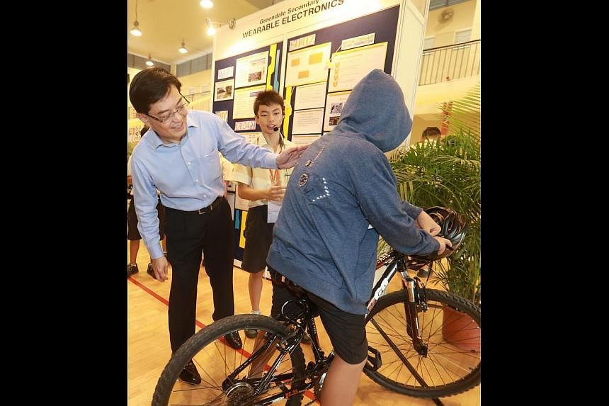Education Minister Heng Swee Keat checking out the "cycling safety jacket" donned by Greendale Secondary School student Lim Xuan Yi, as his group mate Norman Chin, 13, looks on.