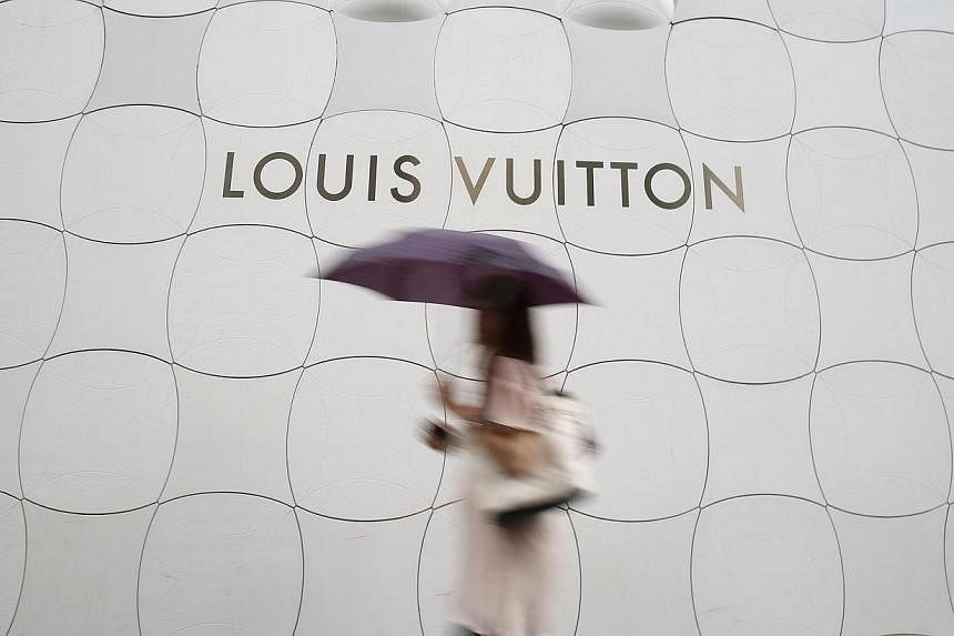A woman holding umbrella walks past a Louis Vuitton logo outside its branch store at Ginza shopping street in Tokyo on Aug 28, 2014.&nbsp;French luxury products group LVMH and Internet search engine Google have agreed to work together to fight the sa