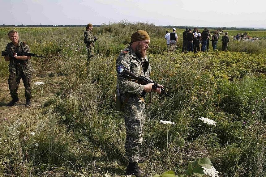 Armed pro-Russian separatists stand guard as monitors from the Organization for Security and Cooperation in Europe (OSCE) and members of a Malaysian air crash investigation team inspect the crash site of Malaysia Airlines Flight MH17, near the villag