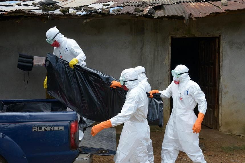 Medical workers of the Liberian Red Cross, wearing a protective suit, carry the body of a victim of the Ebola virus in a bag on Sept 4, 2014, in the small city of Banjol. -- PHOTO: AFP