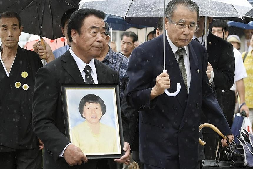 Mr Mikio Watanabe, holding a portrait of his late wife Hamako, walks into the Fukushima District Court in Fukushima, in this photo taken by Kyodo on Aug 26, 2014.&nbsp;The operator of the destroyed Fukushima nuclear power plant said on Friday it won'
