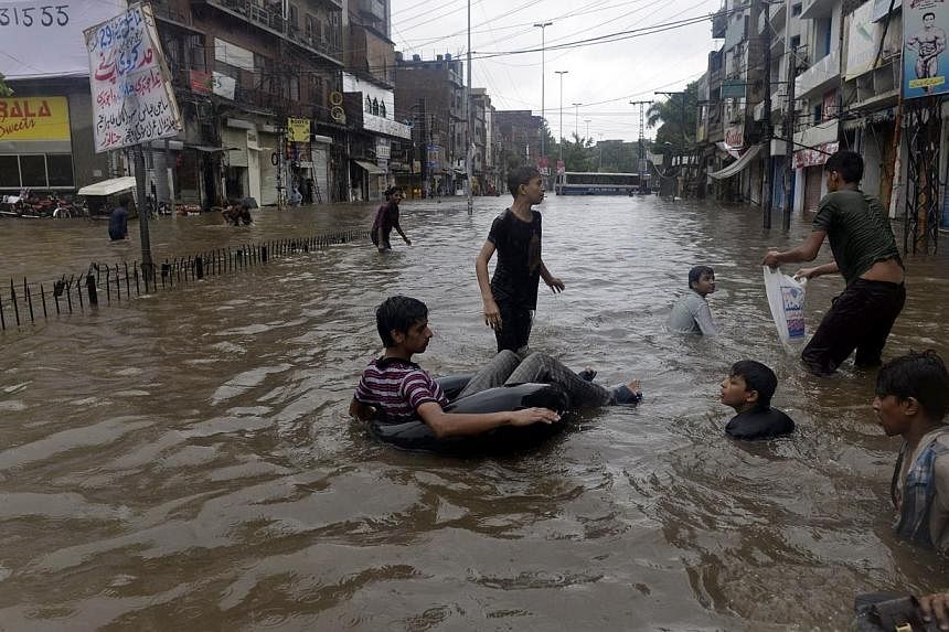 Pakistani youths play in a flooded street during monsoon rain in Lahore on Sept 5, 2014. -- PHOTO: AFP