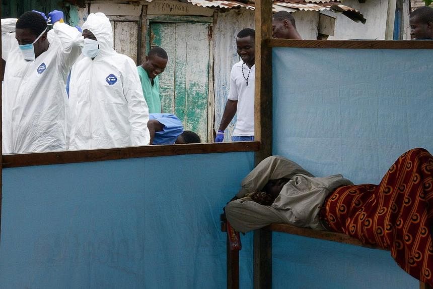 Medical workers of the John Fitzgerald Kennedy hospital in Monrovia, responsible for transport of the bodies of Ebola virus victims, wear their protective suits as they walk past a sick woman waiting for assistance, on Sept 6, 2014. -- PHOTO: AFP