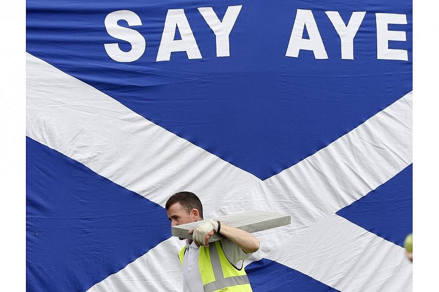 A workman walks past a Scottish saltire in Kilmarnock, Scotland on Sept 3, 2014.&nbsp;The British government is scrambling to respond to a lurch in the opinion polls towards a vote for Scottish independence this month by promising a range of new powe