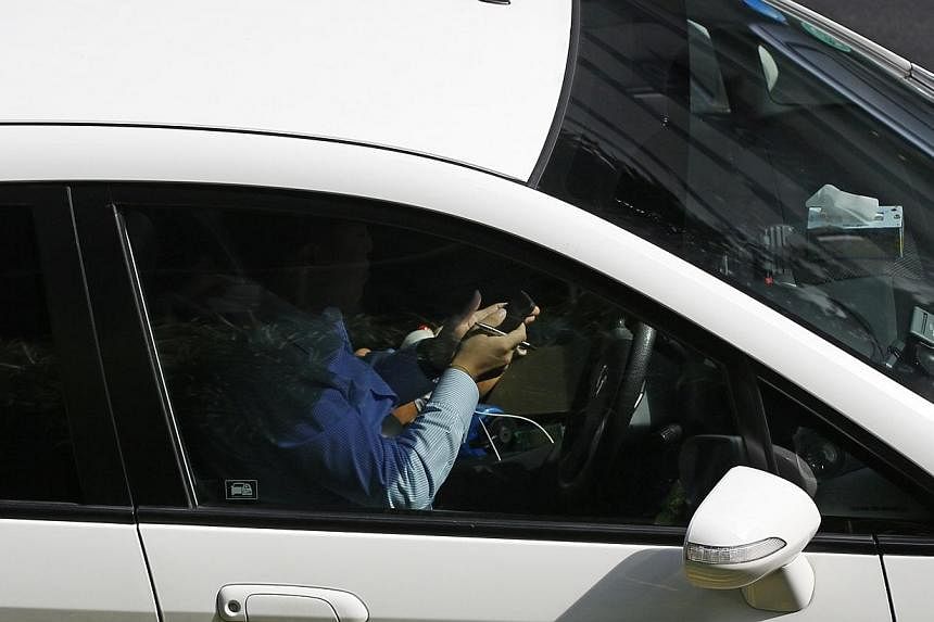 A driver is seen using his mobile phone while driving along Orchard Road. From February next year, motorists caught driving while holding and using any sort of mobile device will be flouting the law. -- ST PHOTO: DESMOND LIU