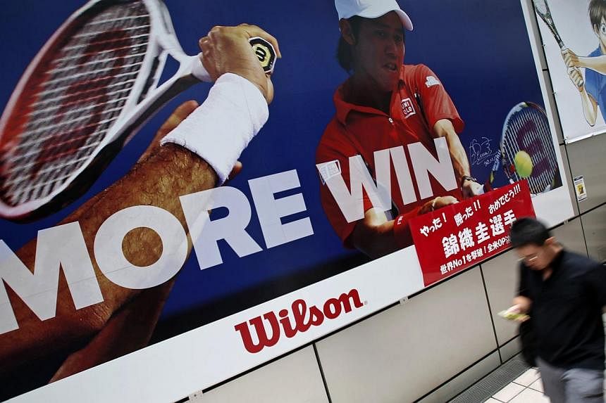A man holding his mobile phone walks in front of a poster of tennis player Kei Nishikori of Japan outside a sports shop in Tokyo on September 8, 2014. -- PHOTO: REUTERS
