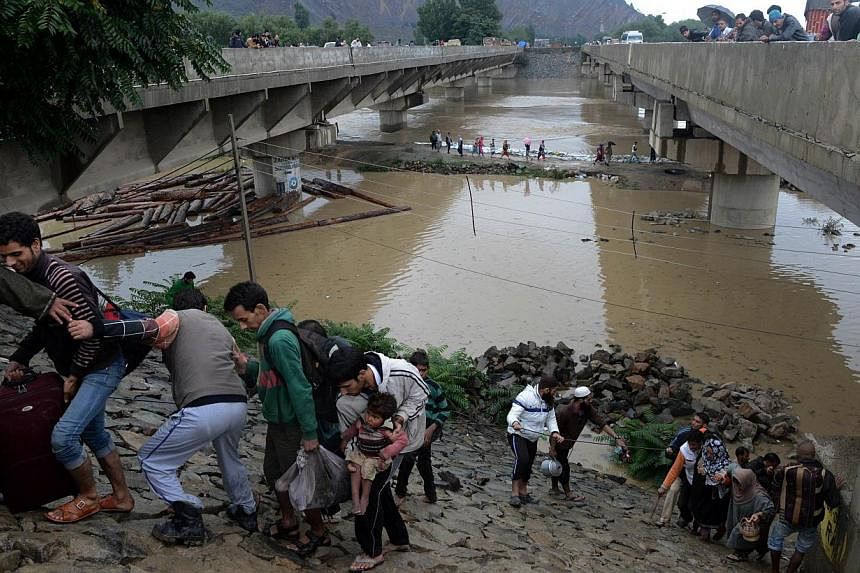 Kashmiri residents walk along an embankment on the side of a bridge as they head for a higher ground during flooding on the outskirts of Srinagar on Sept 6, 2014.&nbsp;Desperate residents were huddled on rooftops on Monday, Sept 8, as they tried to s