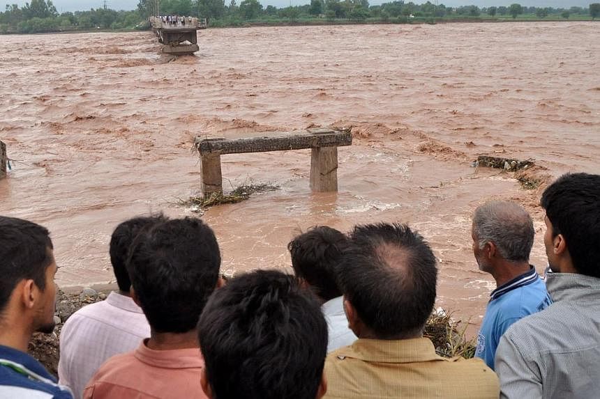 Indian villagers look on at a missing section of a bridge across the overflowing Tawi river that was swept away as flooding continues in the Mandal area of Jammu on Sept 6, 2014.&nbsp;The prime ministers of India and Pakistan have offered to help eac