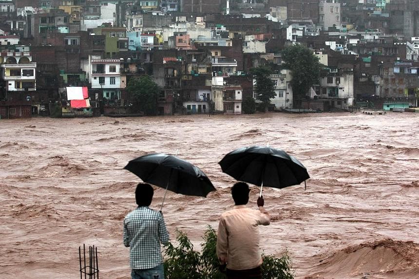 Indian residents look on towards threatened houses as waters from the overflowing Tawi river rage past in Jammu on Sept 6, 2014. -- PHOTO: AFP