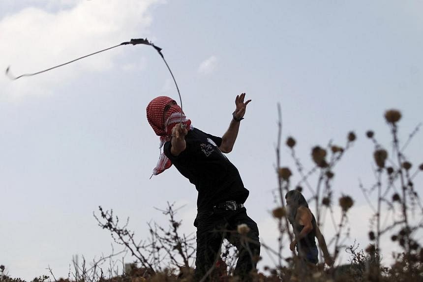 A Palestinian protester uses a sling shot to hurl a stone at Israeli troops during clashes at a weekly protest against Jewish settlements, in the West Bank village of Nabi Saleh, near Ramallah on Sept 5, 2014.&nbsp;A Palestinian was shot dead early o