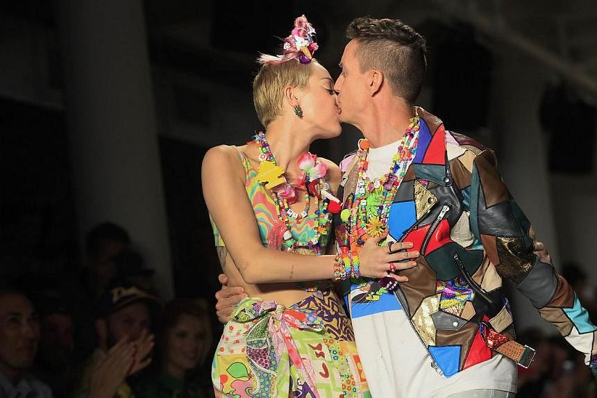Miley Cyrus receives a kiss from Jeremy Scott as they walk the runway during his Spring/Summer 2015 collection at York Fashion Week Sept 10, 2014 in New York.Cyrus teamed up with bad-boy designer Jeremy Scott to unveil a debut art collection for his 