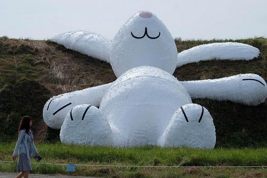 A woman walking past a 25.3-meter-tall giant rabbit, made of plastic and wood and designed by Dutch artist Florentijn Hofman. The rabbit was partially damaged by fire when workers tried to dismantle it. -- PHOTO: AFP