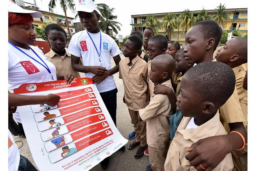 Volunteers wearing t-shirts of the United Nations Development Programme (UNDP) show a placard to raise awareness on the symptoms of the Ebola virus to students of the Sainte Therese school, in the Koumassi district, in Abidjan, on Sept 15, 2014, on t