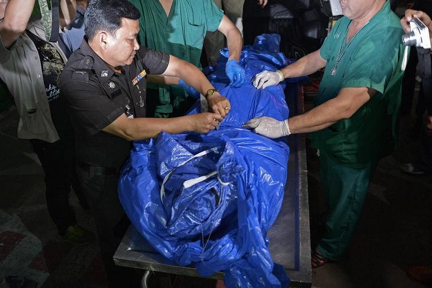 A Thai police officer (left) helps rescue workers pull bags containing the bodies of two murdered British tourists out of a vehicle as they are brought to the forensic department of the Police General Hospital in Bangkok on Sept 16, 2014. -- PHOTO: A