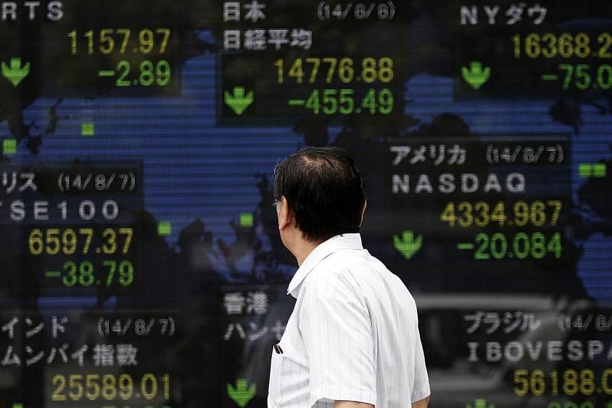 &nbsp;A pedestrian looks at an electronic board showing the stock market indices of various countries outside a brokerage in Tokyo on Aug 8, 2014. -- PHOTO: REUTERS