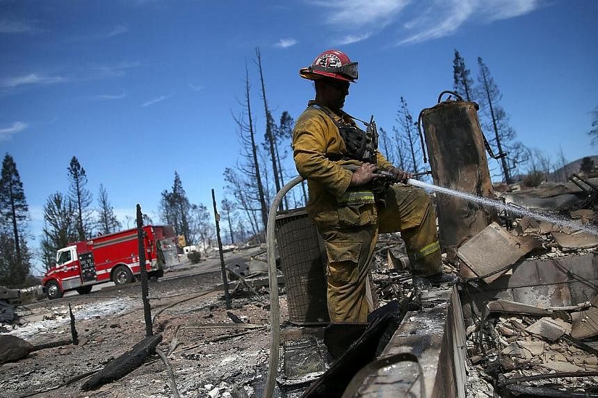 A firefighter cools off hot spots in the remains of a destroyed home in Weed, California on Sept 16, 2014. -- PHOTO: AFP