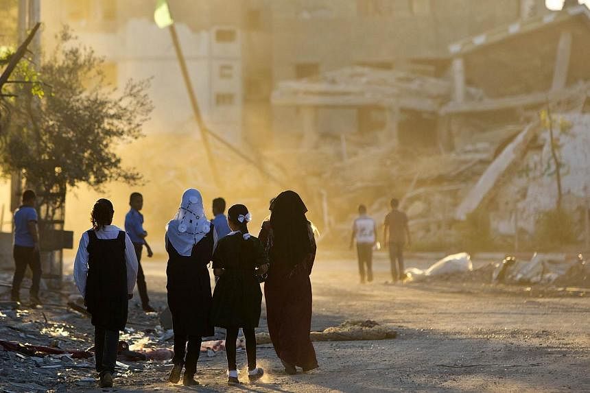 Palestinian girls walk past buildings which were destroyed by Israeli strikes on their way to school in the Shejaiya neighbourhood of Gaza City on Sept 14, 2014 on the first day of the new school year. -- PHOTO: AFP&nbsp;
