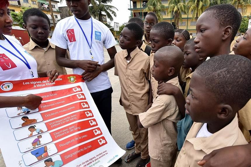 Volunteers wearing t-shirts of the United Nations Development Programme (UNDP) show a placard to raise awareness on the symptoms of the Ebola virus to students of the Sainte Therese school, in the Koumassi district, in Abidjan, on Sept 15, 2014, on t