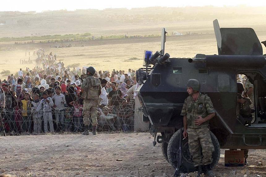 Turkish soldiers stand guard as Syrians wait behind the border fences near the southeastern town of Suruc in Sanliurfa province, on Sept 18, 2014.&nbsp;Close to a thousand Syrian Kurds gathered on the border seeking to cross into Turkey on Friday aft