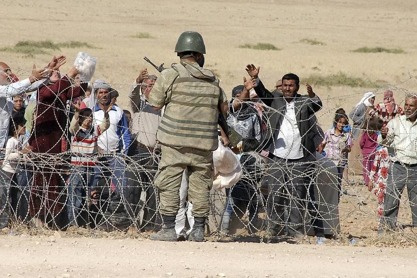 A Turkish soldier stands guard as Syrian Kurds wait behind the border fence to cross into Turkey near the southeastern town of Suruc in Sanliurfa province, on Sept 19, 20 14.&nbsp;Turkey on Friday opened up its border to thousands of Kurds fleeing cl