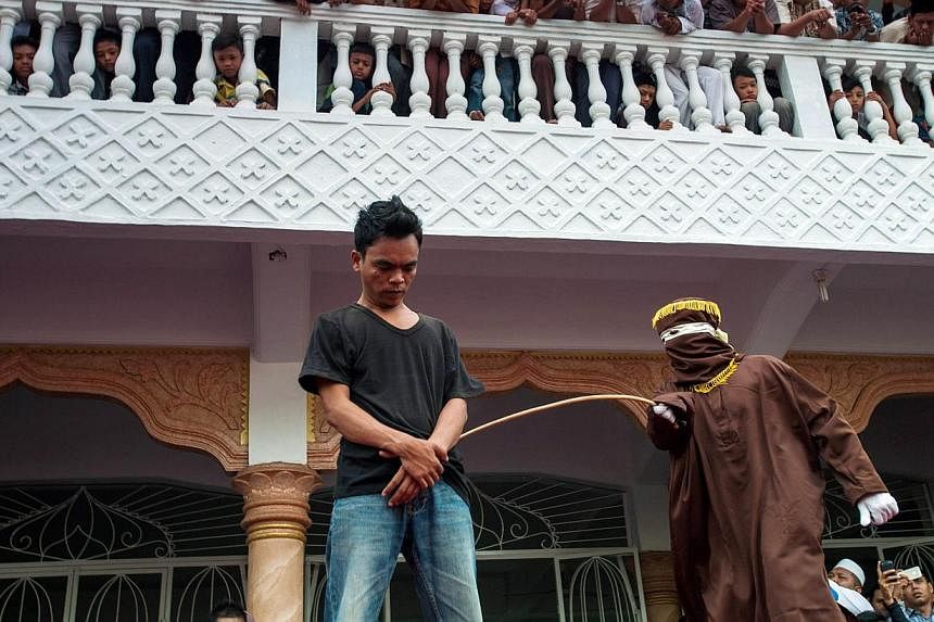 A masked and hooded official (right) canes an Acehnese man for gambling in Banda Aceh on Sept 19, 2014. Gay sex could be punishable by 100 lashes of the cane in Indonesia's staunchly conservative Aceh province if Parliament passes a draft law that cr