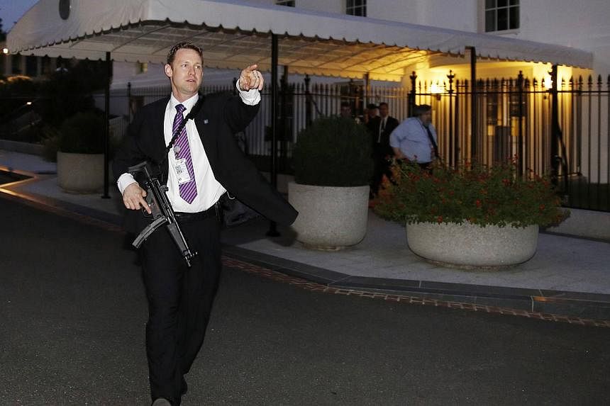 A US Secret Service agent with an automatic rifle hurries people to evacuate the White House complex over a security alert moments after President Barack Obama and his family left for the presidential retreat, Camp David, in Maryland on Sept 19, 2014