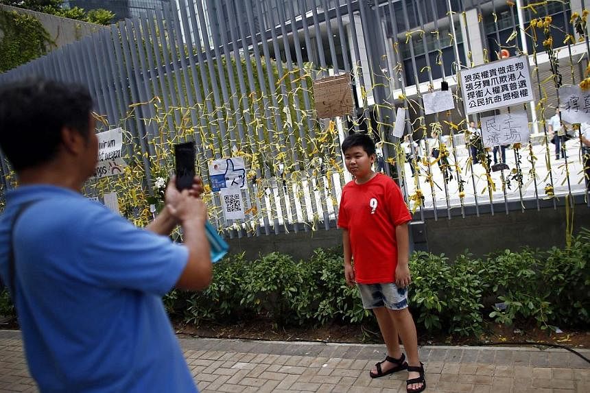 A man take pictures of his son, standing near a fence adorned with yellow ribbons and messages in support of the pro-democracy demonstrations, in front of the government headquarters as protesters block the surrounding areas in Hong Kong on Oct 2, 20